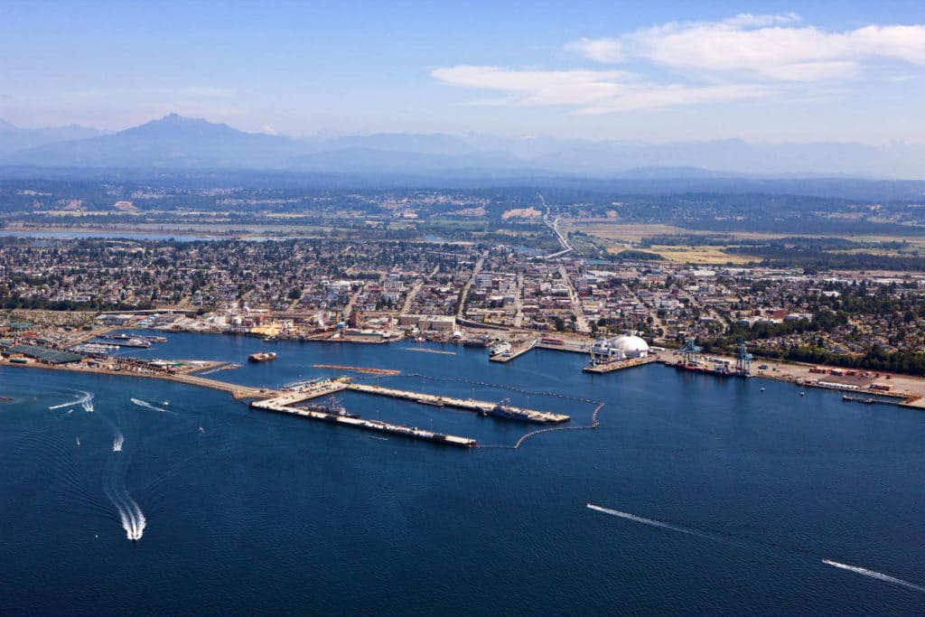 Aerial view of Everett, WA waterfront with docks, boats, and mountains in the background.