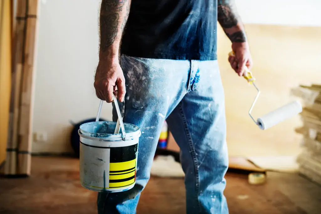A painter holding a bucket of blue paint and a roller, ready to start an indoor painting project. Includes small space deck ideas Bellevue for outdoor spaces.