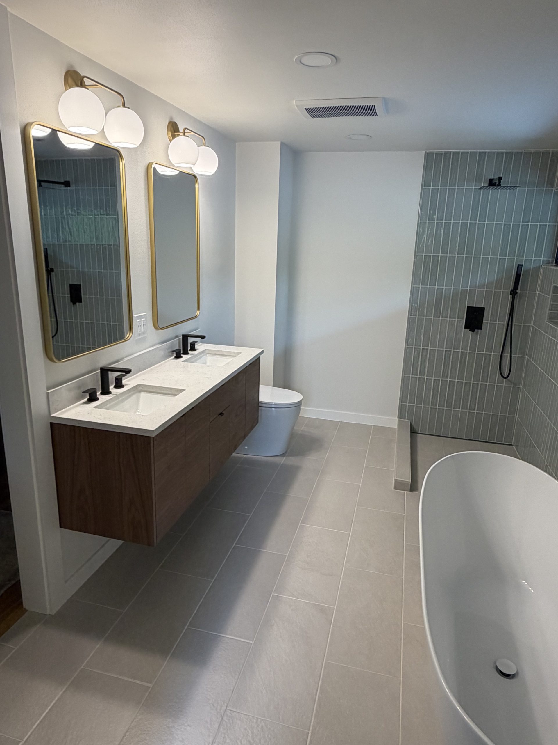 Completely remodeled bathroom with floating wood double vanity, gold mirrors, walk-in shower with black fixtures, and freestanding bathtub — YSG Construct