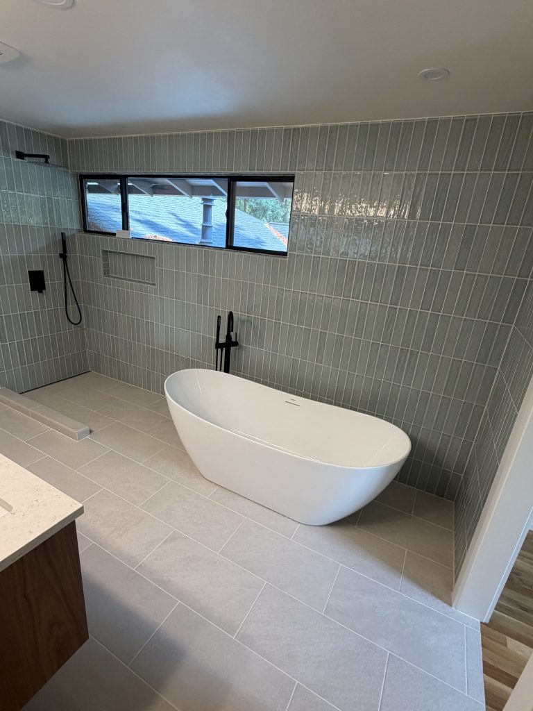 Freestanding bathtub beside a walk-in shower with vertical tile and matte black fixtures