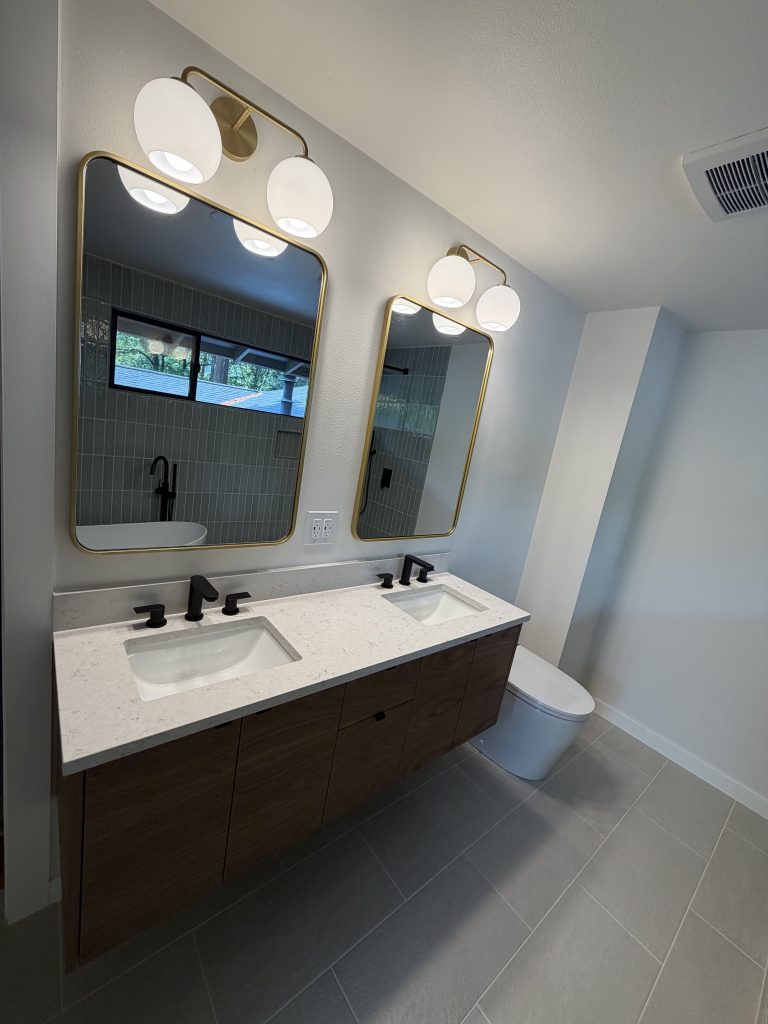 Floating wood double vanity with gold-framed mirrors and globe sconce lighting