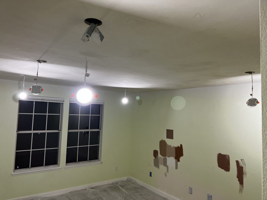 Recessed can lights being installed in freshly skim-coated ceiling