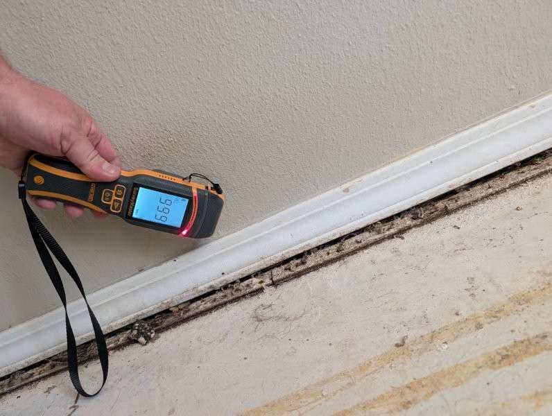 Moisture meter held at a basement baseboard — water damage restoration in Brier, WA by YSG Construct