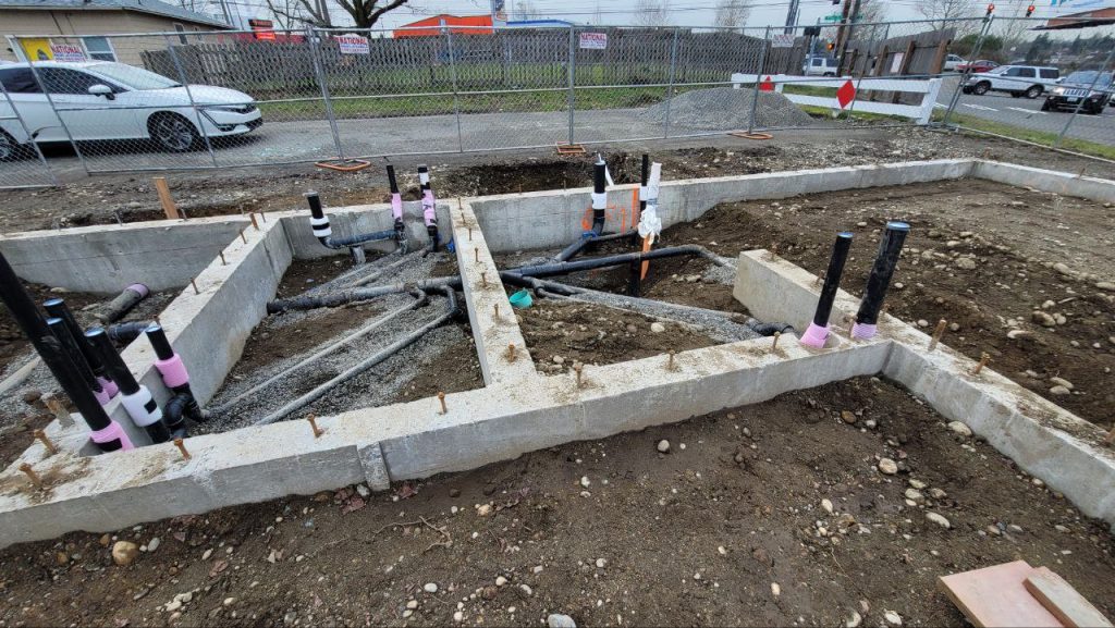 Corner of poured concrete strip footings with underground sewer lines in trenches in Tacoma WA by YSG Construct