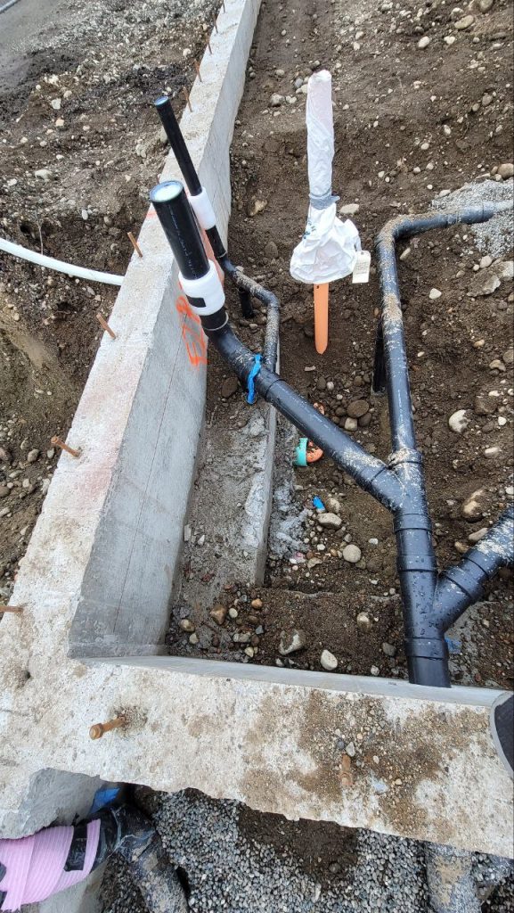 Underground sewer pipes laid in trench alongside concrete footing with roughed-in stacks in Tacoma WA by YSG Construct