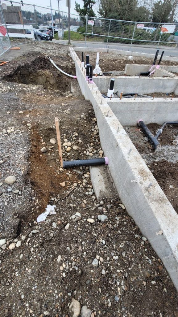 Black utility pipe penetrating through concrete footing wall with sleeved seal in Tacoma WA by YSG Construct
