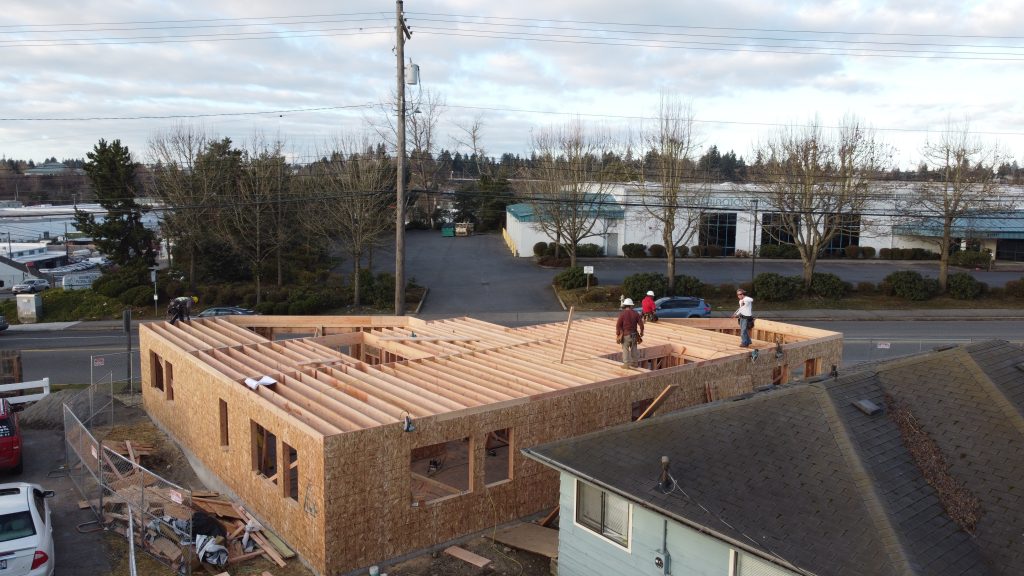 Framed walls with sheathing and workers installing roof framing on a new construction site — YSG Construct
