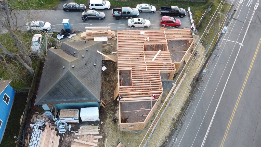 Aerial view of complete house floor framing with lumber stacks and crew on site — YSG Construct