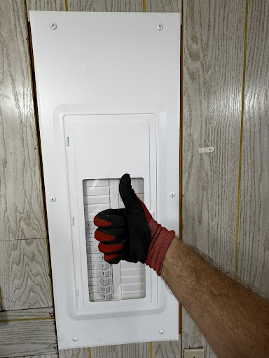Gloved hand pointing to newly installed electrical panel cover on wood wall